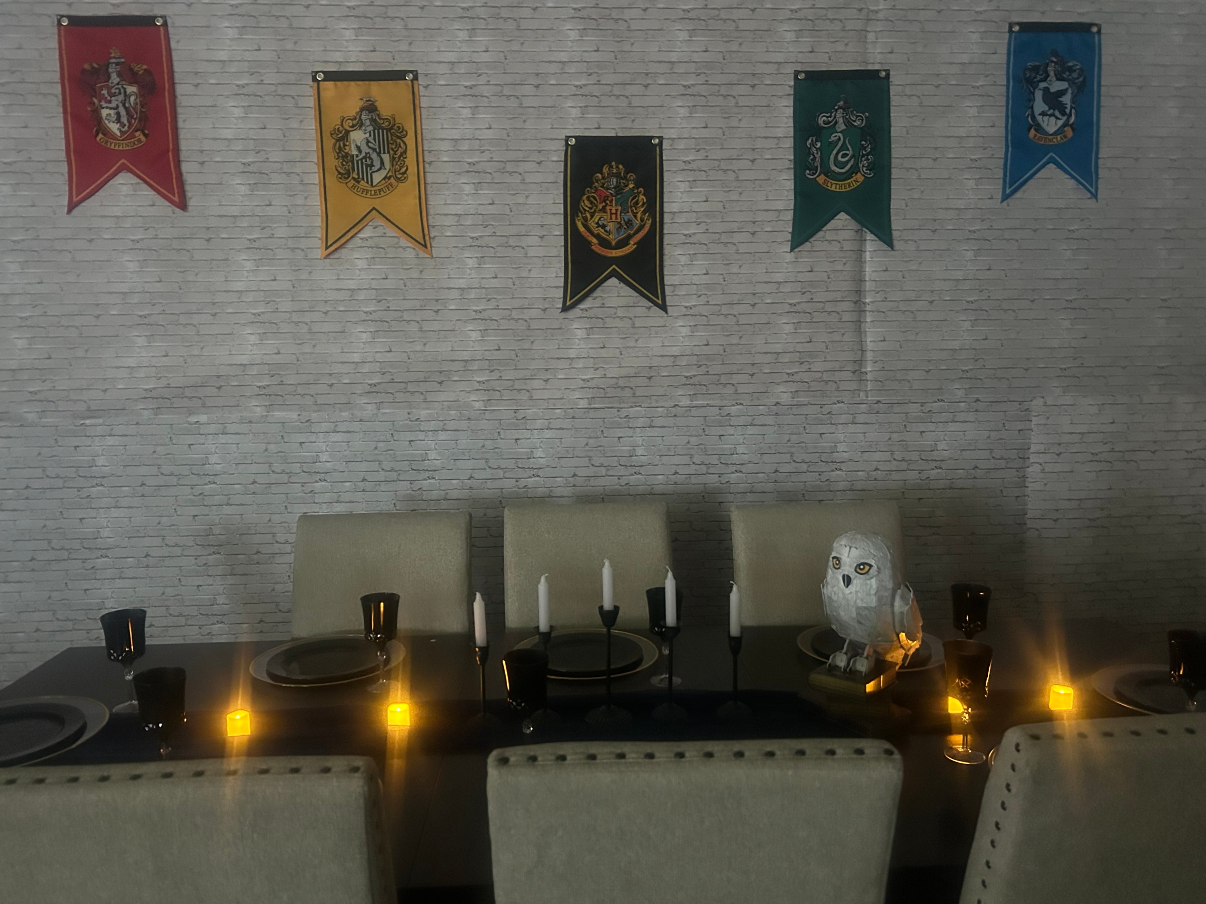 Wide view of a Harry Potter themed event room with house banners, candelabra, Hedwig owl and black Happy Birthday balloon letters on the wall