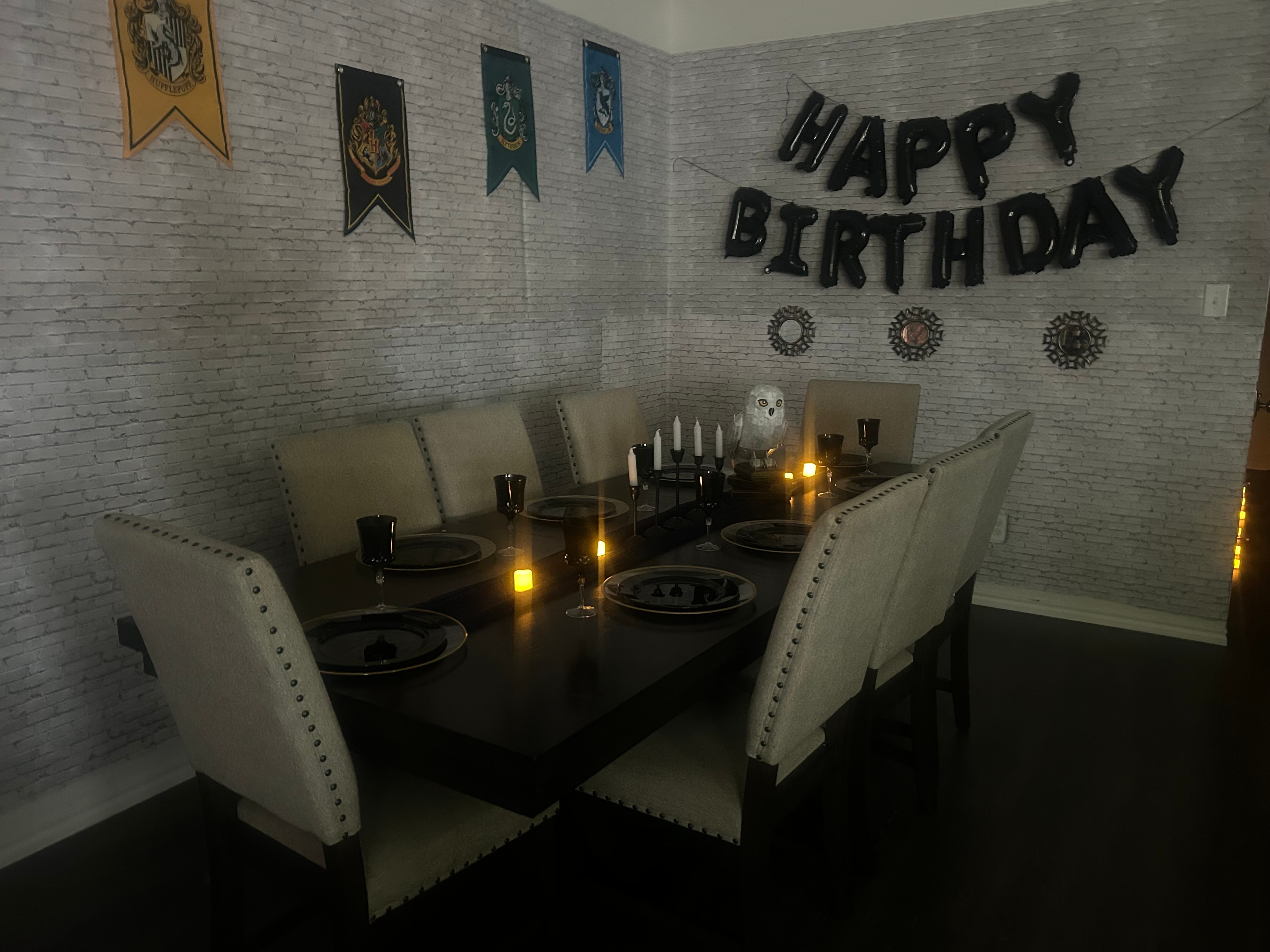 Close-up of a Harry Potter themed dining table with Gryffindor, Hufflepuff, Hogwarts, Slytherin and Ravenclaw house banners, candelabra and Hedwig owl decoration